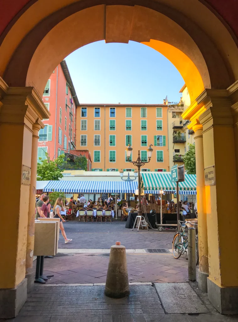 Passage voûté ouvrant sur une place animée du Vieux-Nice